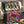 A plush throw blanket draped over a cream armchair, featuring a colorful 'Salty Mermaid' sardine can design with mermaid artwork and fish illustrations. The blanket has a dark green velvet-like border and a bright pink center panel.