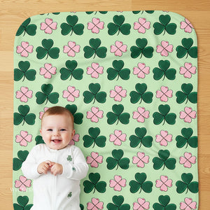 Baby lying on a green mat with shamrock pattern, smiling at the camera.