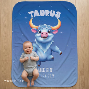 Baby sitting on a blue blanket with a cartoon Taurus character and text.