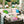 Outdoor patio scene with a wicker sofa set decorated with pastel pillows and throws, next to a decorated Christmas tree and large colorful ornaments in the background. A 'Wicked Cat' watermark appears in the lower left.