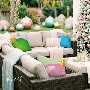 Outdoor patio scene with a wicker sofa set decorated with pastel pillows and throws, next to a decorated Christmas tree and large colorful ornaments in the background. A 'Wicked Cat' watermark appears in the lower left.