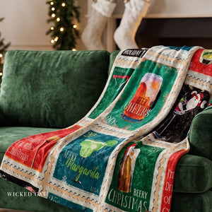 A festive Christmas-themed throw blanket draped over a green velvet couch in a cozy living room setting. The blanket features a patchwork design of vintage-style beer and cocktail posters with text like 'Beer Cheers', 'Margarita', 'Berry Christmas', and 'Happy Holidays'.