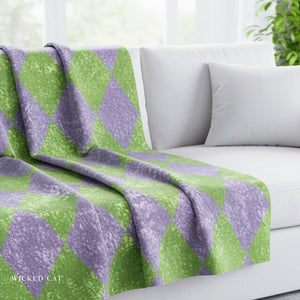 Green and purple patterned blanket draped over a white sofa with a blurred background