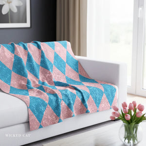 Pink and blue geometric patterned blanket on a white couch with a vase of flowers in the background.