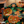 A Halloween-themed throw blanket draped over an armchair in a cozy indoor setting. The blanket features a repeating pattern of orange jack-o'-lantern pumpkins with glowing yellow eyes and mouths on a black background with green leaves.