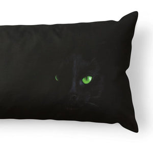 A black rectangular throw pillow featuring a printed design of a black cat with glowing green eyes, shown against a plain white background.