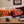 Two rectangular throw pillows on a beige couch in a living room setting. One pillow is bright orange with dark purple text reading 'EXIT LIGHT', and the other is dark maroon with orange text reading 'ENTER NIGHT.