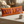 An orange rectangular throw pillow with the words 'EXIT LIGHT' printed in large distressed purple letters, resting on a beige tablecloth in a softly lit living room. A ceramic mug sits nearby, and the brand name 'WICKED CAT' appears in the lower left corner.