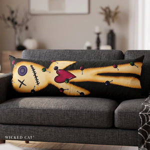 A long rectangular throw pillow featuring a stitched voodoo doll design in yellow, black, red, and purple, resting on a gray fabric sofa in a living room setting. The brand name 'Wicked Cat' is visible in the bottom left corner.