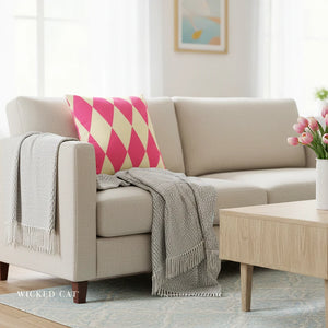 Beige sofa with a pink and white patterned pillow, gray blanket, and wooden coffee table in a living room setting.