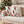 Two square throw pillows with a red and cream candy cane pattern, styled on a textured beige armchair in front of a decorated Christmas tree.