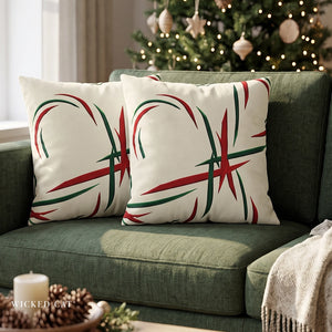 Two square throw pillows with a red and green abstract leaf pattern on an off-white background, styled on a green sofa in a cozy living room setting with a Christmas tree in the background.