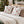 Two square decorative throw pillows with a white background and a red, blue, and green martini glass pattern, styled on a bed with beige sheets and pillows in a cozy holiday bedroom setting with a decorated Christmas tree in the background.