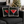 Two square throw pillows with a Christmas-themed 'Merry Martini' stamp design, styled on a dark gray sofa with a blurred Christmas tree in the background.