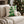 A square decorative throw pillow with a green holly and white cloud-like border design, resting on a light beige sofa in a cozy living room setting with a Christmas tree in the background. The brand name 'WICKED CAT' is visible in the bottom left corner.