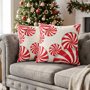 Two Christmas throw pillows with red peppermints on a grey couch in a living room decorated for the holidays.