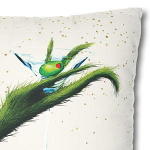A square throw pillow featuring a festive Grinch-inspired illustration of a green arm holding a martini glass with an olive, set against a cream background with gold speckles and a red-and-white corner detail.
