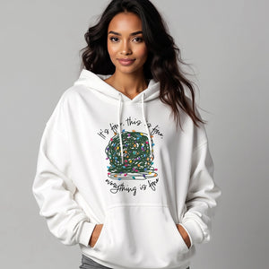 woman wearing a white sweatshirt hoodie with a graphic of a ball of tangled Christmas lights and text that says 'It's fine, this is fine, everything is fine'.
