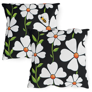 Two square accent pillows with a black background featuring a white floral pattern and a small bumble bee design.