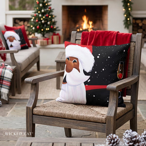A festive Christmas throw pillow featuring a cartoon Santa with a white beard and black hat, resting on a wooden outdoor chair in front of a cozy fireplace. The chair also has a red blanket draped over it, and other holiday decorations are visible in the background.