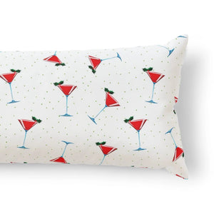 A rectangular lumbar pillow with a white background printed with a festive pattern of red martini glasses, green dots, and small green sprigs, shown on a clean white background.