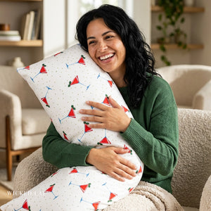 A woman smiling while hugging a white lumbar pillow with a red and green cocktail martini print, sitting in a cozy living room setting.