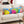 A long rectangular lumbar pillow with a colorful Christmas ornament and gift box pattern, resting on a light beige sofa in a cozy living room setting.