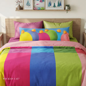 A colorful bedding set styled on a bed in a bedroom setting, featuring a duvet cover with vertical stripes of pink, blue, and lime green, matching pillowcases, and a decorative throw pillow with a colorful holiday ornaments . The brand name 'WICKED CAT' is visible at the bottom left corner.