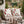 Two white outdoor throw pillows with a red candy cane pattern, styled on a wicker patio chair next to a beige knit blanket, with a festive garden background.
