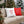 Two square throw pillows on a wicker sofa: one white with a red candy cane heart motif and one red with a white candy cane heart motif, set outdoors in front of a decorated Christmas tree.