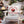 A white Adirondack chair at a holiday outdoor gathering, featuring a square throw pillow with a red and white graphic that reads 'CANDY CANES ROASTERS NORTH POLE GROWN LIMITED EDITION' with an illustration of a coffee cup.