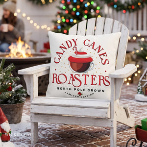 A white Adirondack chair at a holiday outdoor gathering, featuring a square throw pillow with a red and white graphic that reads 'CANDY CANES ROASTERS NORTH POLE GROWN LIMITED EDITION' with an illustration of a coffee cup.
