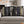 Two black throw pillows with a gothic book spine collage design, displayed on a light gray sofa in a cozy living room setting with warm string lights in the background.