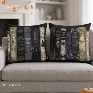 Two black throw pillows with a gothic book spine collage design, displayed on a light gray sofa in a cozy living room setting with warm string lights in the background.