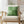 Green checkered pillow on a beige armchair in a bright room with plants and decor.