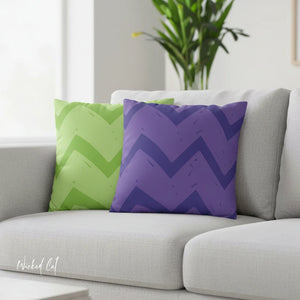 Green and purple chevron-patterned pillows on a gray sofa with a plant in the background.