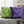 Green and purple chevron-patterned pillows on a gray couch with a blurred background.