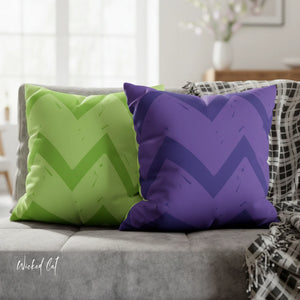 Green and purple chevron-patterned pillows on a gray couch with a blurred background.