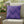 Purple zigzag patterned pillow on a beige chair with outdoor plants in the background