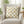 Decorative pillow with bee pattern on a chair in a room with plants and a table.