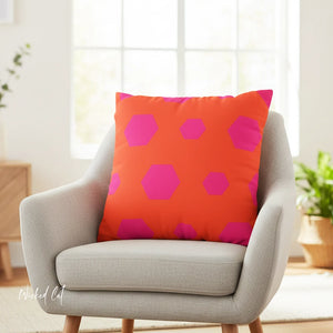 Orange pillow with pink geometric pattern on a gray chair in a bright room.