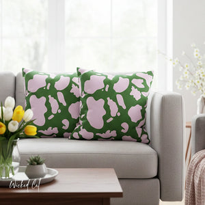 Green and pink abstract patterned pillows on a gray sofa with a wooden coffee table and flowers.