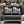 Two black outdoor throw pillows with bold white 'FALALALALALALALALA' text and small white snowflake accents, displayed on a gray outdoor sofa with holiday decorations in the background.