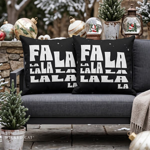 Two black outdoor throw pillows with bold white 'FALALALALALALALALA' text and small white snowflake accents, displayed on a gray outdoor sofa with holiday decorations in the background.