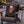 A black decorative throw pillow featuring a vintage-style beer label design for 'North Pole Festivus Ale' by Wicked Cat, displayed on a wooden Adirondack chair in an outdoor patio setting.