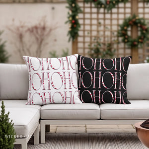 Two decorative throw pillows with a repeating 'HO HO HO' candy cane pattern, styled on a white outdoor sectional sofa. One pillow is white with red lettering, and the other is black with red lettering.
