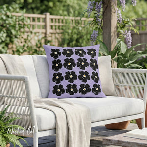 Decorative pillow with black floral pattern on a white outdoor sofa with greenery in the background