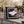 A square black throw pillow with a postage stamp design featuring a Christmas-themed margarita, resting on a weathered wooden chair in a festive outdoor setting with blurred Christmas lights and a tree in the background.