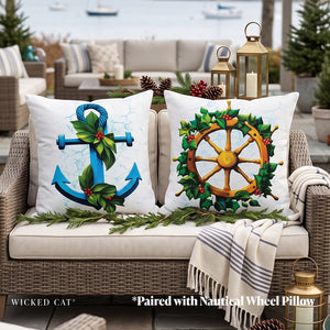 Two decorative outdoor throw pillows displayed on a wicker patio sofa. One pillow features a blue anchor with green holly leaves and red berries on a white background.