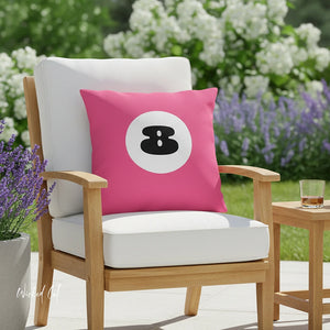 Pink pillow with a black number 8 design on a white cushioned chair outdoors.